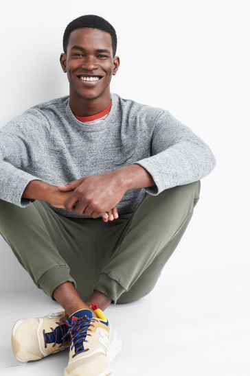 Man wearing a grey workout top, dark earth tone sweat pants and shoes.