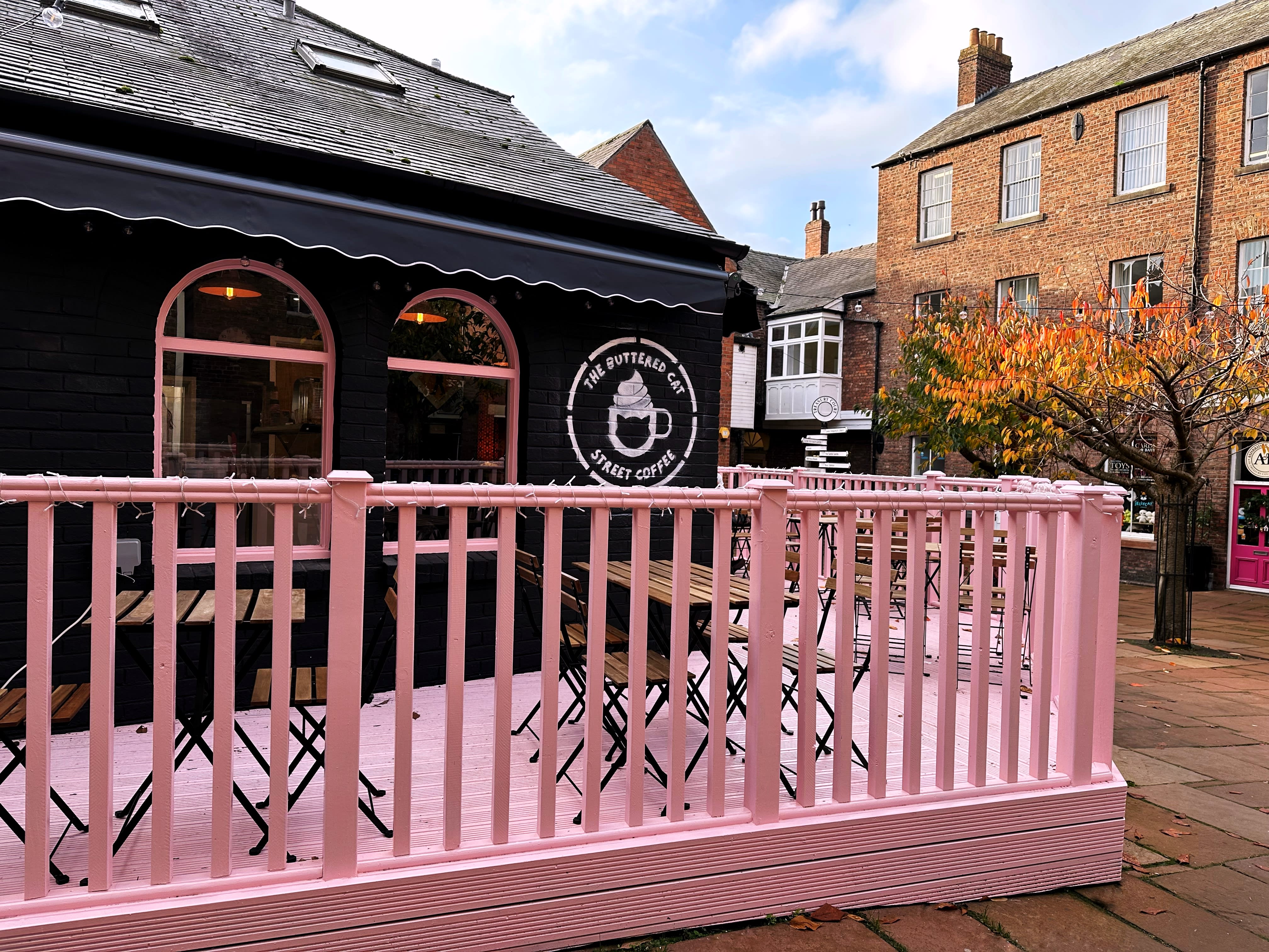 The black frontage with pink arched windows and a scalloped awning, and outdoor tables on the pink decked terrace beside the brick buildings of Treasury Court.