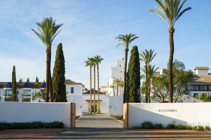 Witte ingang van een wit hotel van Zuid-Spaanse inspiratie, hoge palmbomen en cipressen verwelkomen de gasten