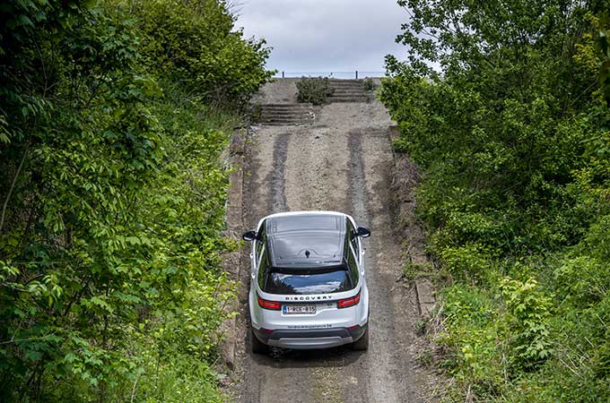 Un Discovery blanc monte une pente montagneuse couverte de feuillage.
