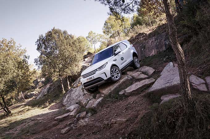Un Discovery blanc garé sur des rochers escarpés dans les bois.