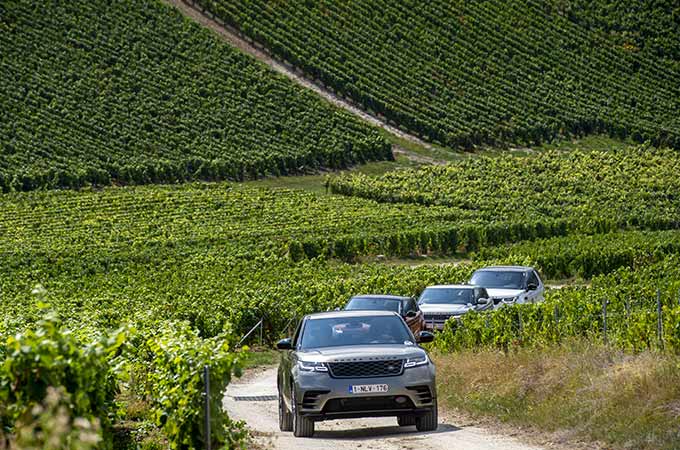 Quatre véhicules roulant en file sur une route de campagne verdoyante.