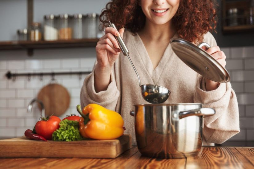 Photo of attractive caucasian woman holding cooking ladle spoon while eating soup with fresh vegetables in kitchen at home