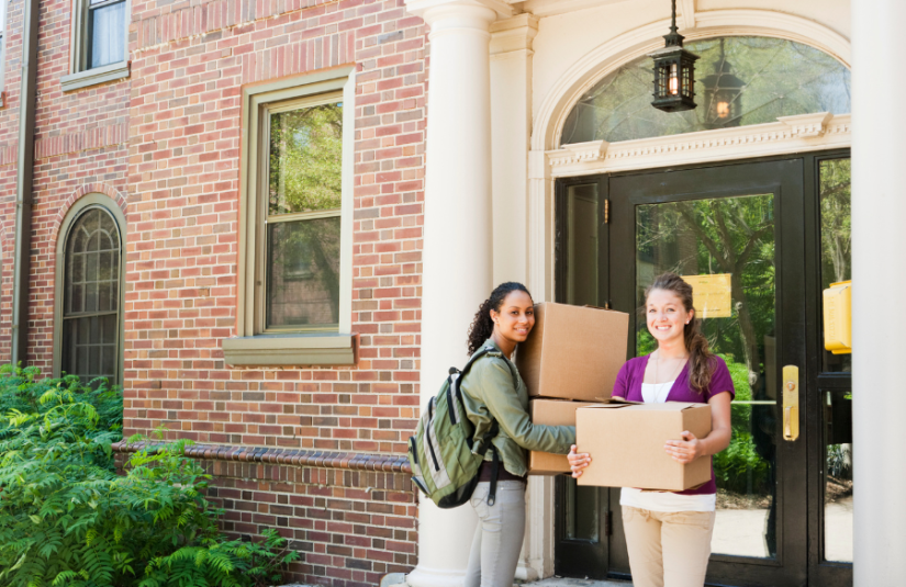 Two girls holding a boxes in front of a door