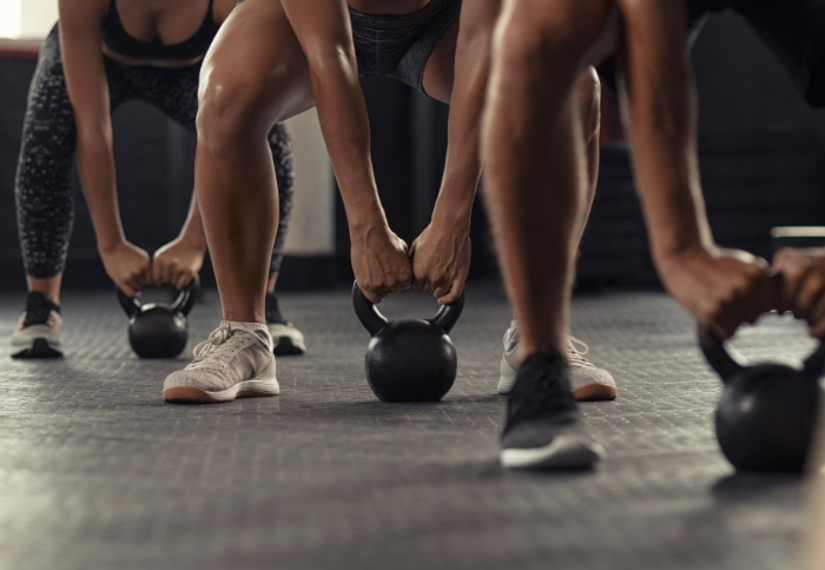 A row of people in workout clothes, lifting kettlebells.