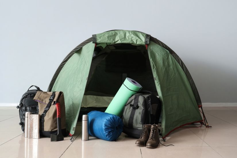 A tent, sleeping bag, and other gear set out on a home floor.