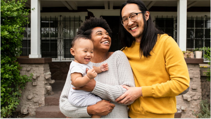 family wearing yellow and gray standing outside of a home holding a baby