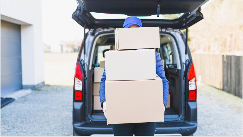 person wearing blue holding boxes vertically outside of an open car trunk