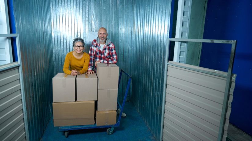 Couple standing beside stacked moving boxes inside a self-storage unit.