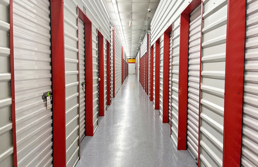 The interior hallway of a storage facility, with white storage unit doors accented by pops of red.