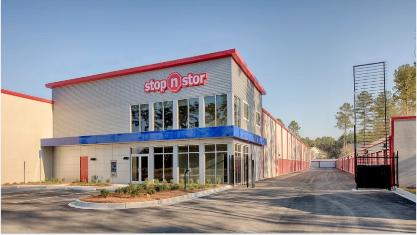 Stop N Stor facility with red roof and blue strip above doors with black open gate and drive up storage units with red storage unit doors
