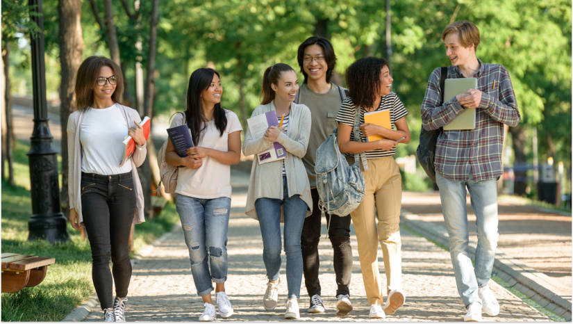 students walking on a college campus smiling and talking holding notebooks
