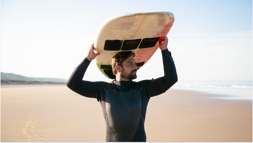 guy on the beach in a wetsuit with a surfboard above his head