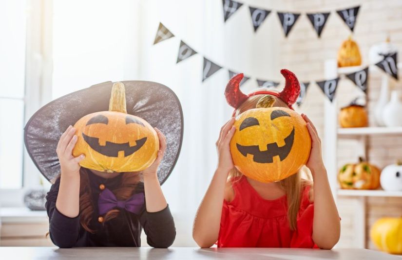 Two children in Halloween costumes holding jack-o'-lanterns in front of their faces.