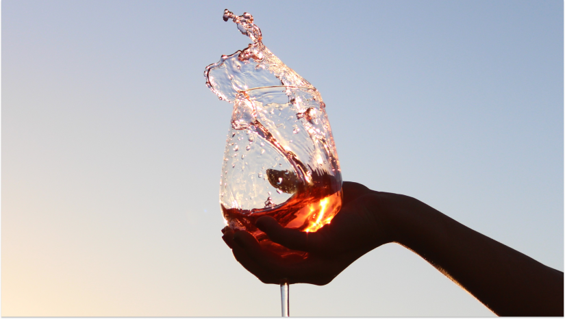 silhouette hand splashing a glass of wine in front of a sunset