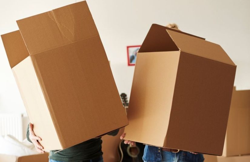 Two people holding moving boxes that block their faces.