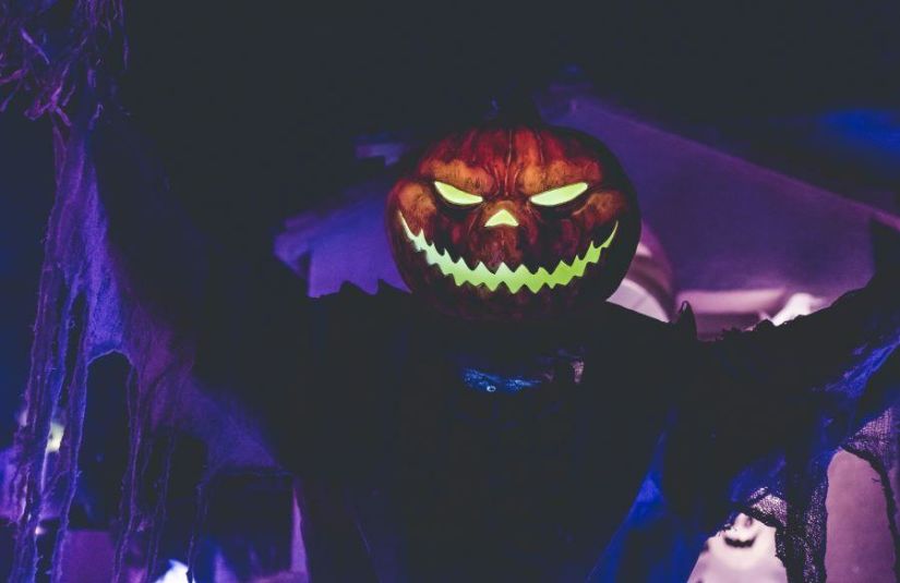 A person in a spooky costume with a glowing jack o'lantern head looms towards the camera.