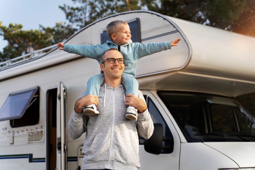 man with child on shoulders with rv in background