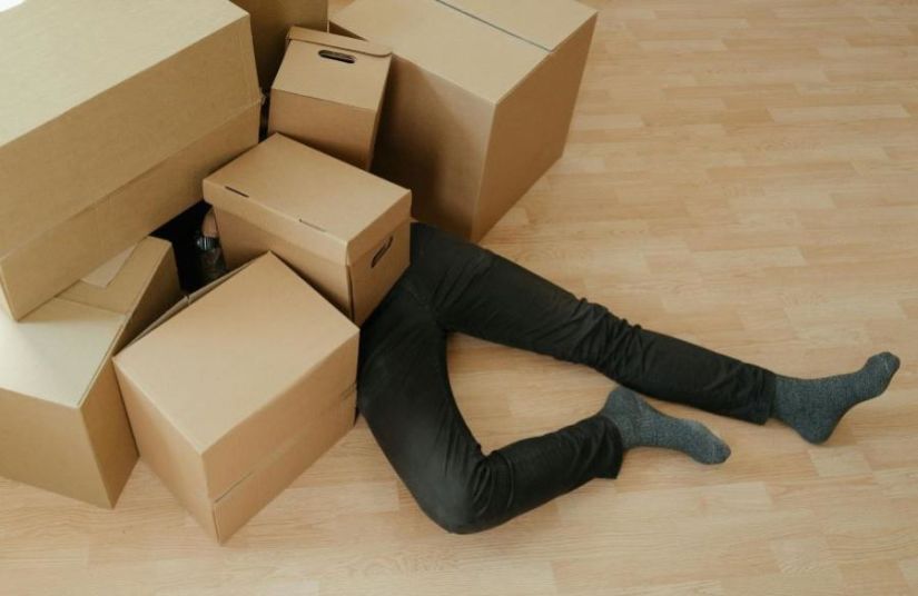 A person being buried under a pile of cardboard boxes.