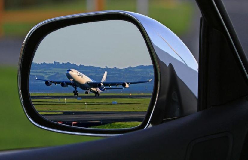 An airplane on the tarmac, as seen in the rearview mirror of a car