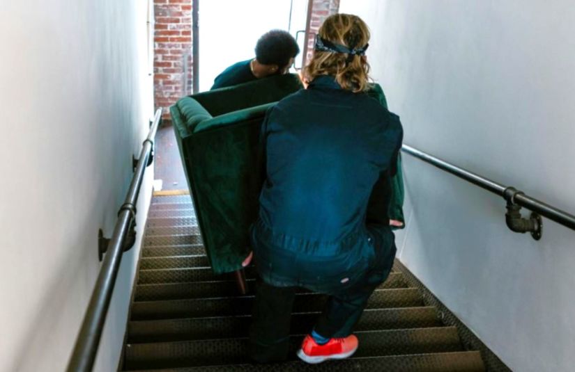 Two movers carry a sofa up a staircase.