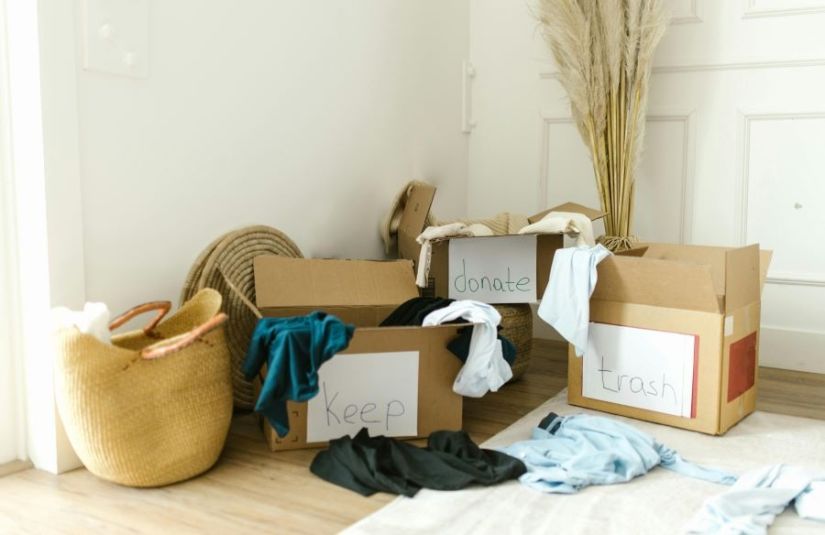 Cardboard boxes labeled "keep," "donate," and "trash." Clothes spill out of the boxes.