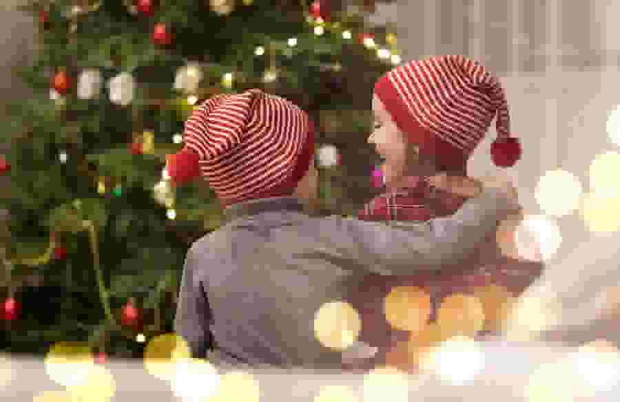 A little boy and little girl sitting in front of a Christmas tree smiling at each other