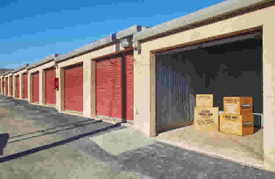 A row of drive-up storage units. One unit is open and several cardboard boxes are visible inside.