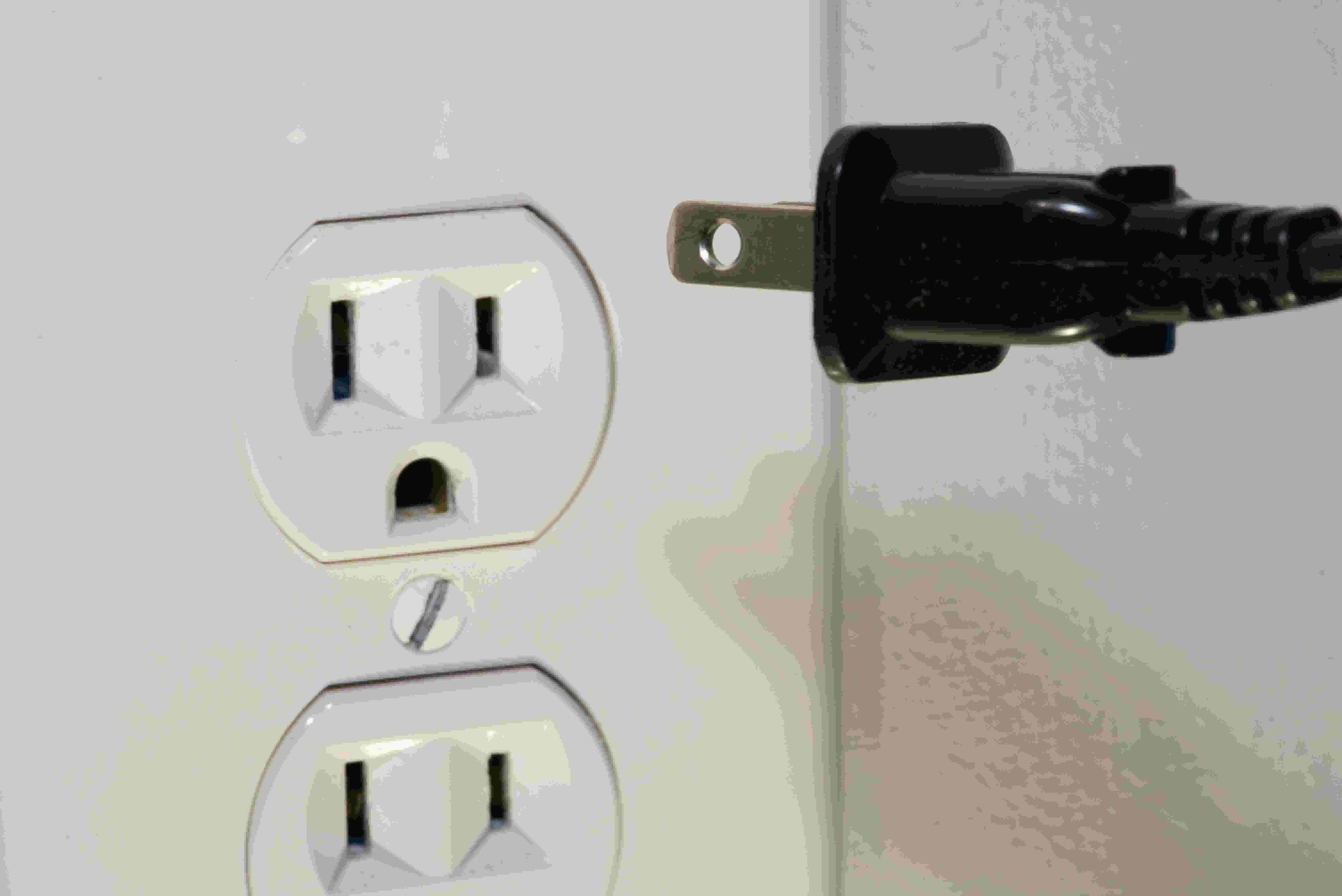 A black plug being plugged into a wall socket.