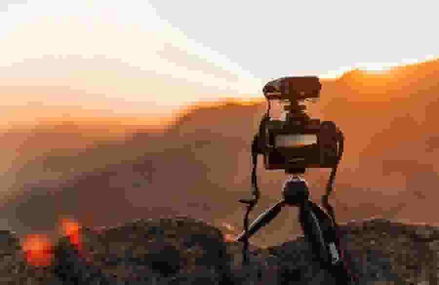 A camera perched on a rock, taking a picture of the sun setting over a mountain range.