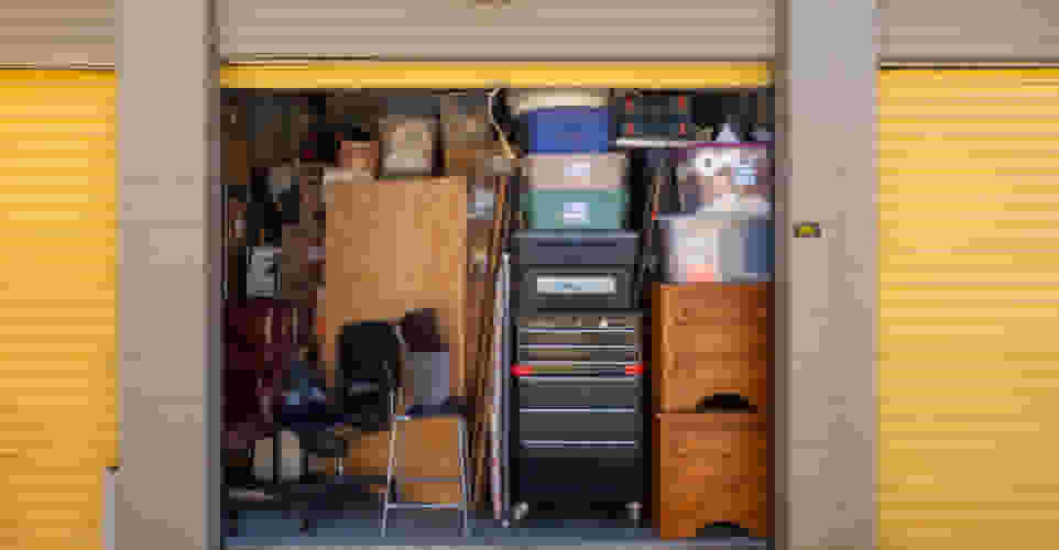Very full storage unit with chairs, a table, a filing cabinet, dressers and containers
