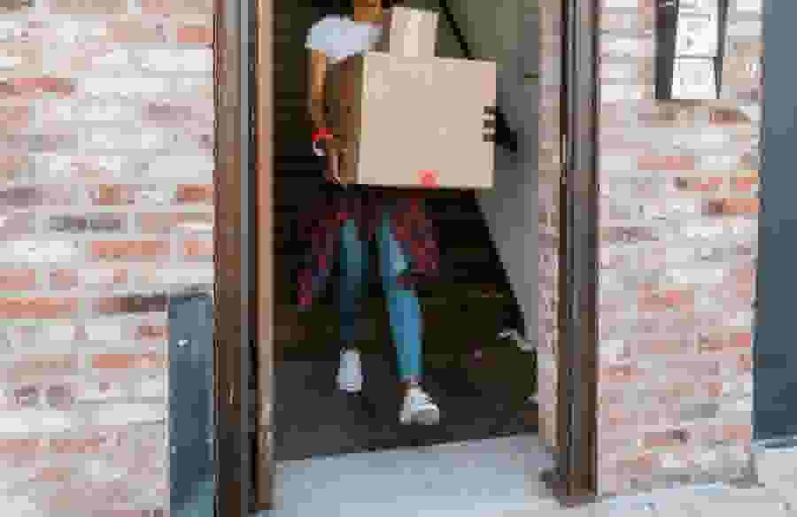 A college student carries boxes down the stairs and out the front door.