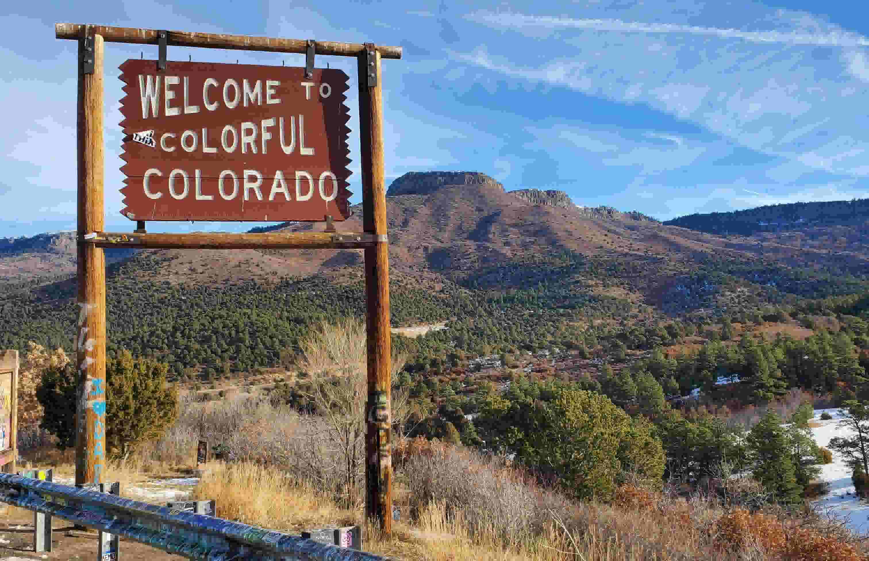 A sign that says "Welcome to Colorful Colorado." The sign stands in front of a beautiful landscape.