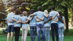 Group of diverse volunteers with arms around each other in matching light blue shirts standing in a park