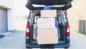 person wearing blue holding storage boxes vertically outside of an open car trunk