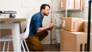 man wearing blue and brown courhcing on floor and taking notes while looking at storage boxes