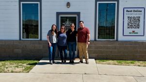 A small team of four people standing in front of a self-storage office while smiling.
