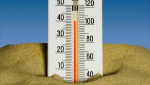 A thermometer buried in the sand against a blue sky. The temperature on the thermometer is over 100 degrees Fahrenheit.