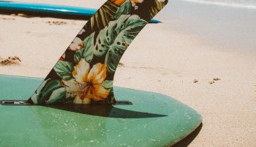 A surfboard resting on the sand at the edge of the ocean.