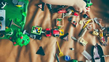 A pile of toys on a bed. A child is grabbing one of the toys.