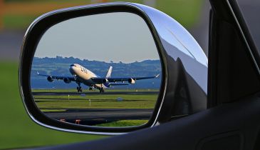 An airplane on the tarmac, as seen in the rearview mirror of a car