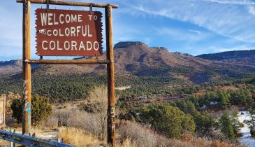 A sign that says "Welcome to Colorful Colorado." The sign stands in front of a beautiful landscape.