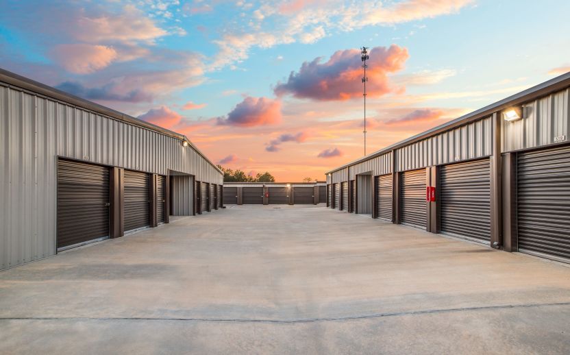 Rows of drive-up storage units. A beautiful sunset is visible behind the buildings.