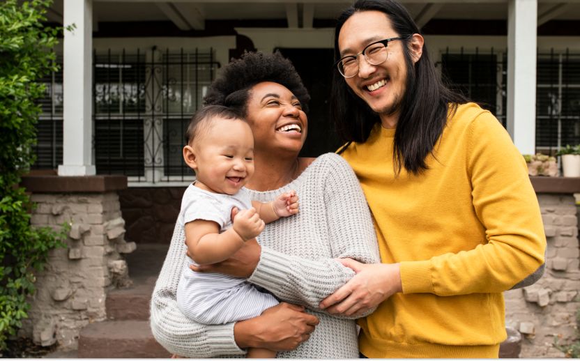 family wearing yellow and gray smiling outside a home with a baby