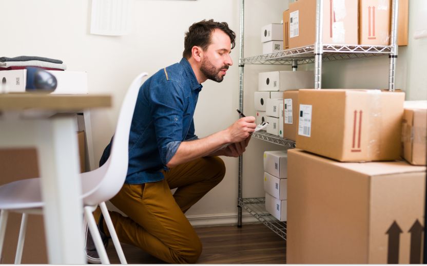 man crouching on floor looking at storage boxes and taking notes