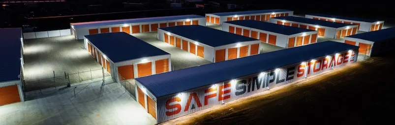 An aerial view of Safe Simple Storage at dusk, with bright lights illuminating the rows of secure, drive-up storage units.
