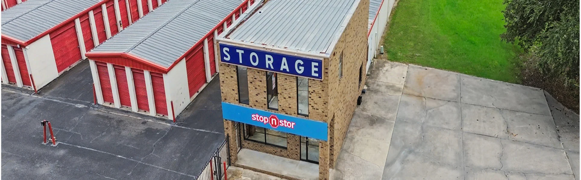 Brown Stop N Stor building with "storage" written on a blue banner, next to drive up storage units with red roll up storage unit doors.
