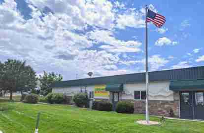 The front office of the property. An American flag is flying on a flagpole in front of the office building, which has an illuminated 'Open' sign.