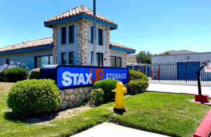 The front of the property. The front office and gated entrance are visible, as well as the entry keypad for the gate. A StaxUP Storage sign is in front of the facility.