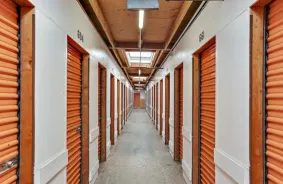 A clean, well-lit interior hallway lined with orange storage unit doors.